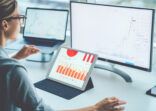 Rear view of woman financial specialist studying theory and practice blockchain technology. Female broker sitting front computer with graphs statistics of stock exchange. Earnings on raising quotes